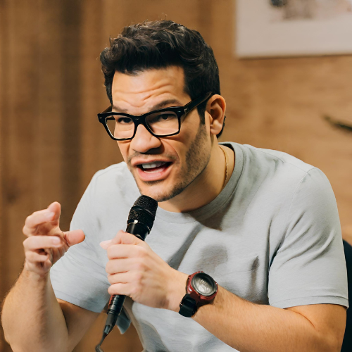 Tai Lopez passionately delivering a speech about the importance of mentors in personal and professional growth. He stands confidently on a well-lit stage with a microphone in hand, engaging the audience with his insightful wisdom and energetic demeanor.